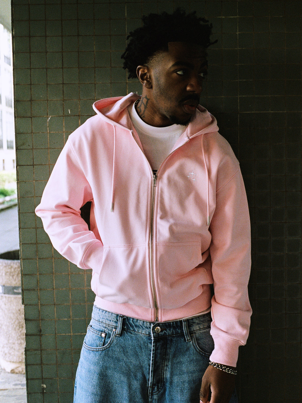 Model wearing a baby pink Drama Call STA zip-up hoodie in an outdoor lifestyle view.