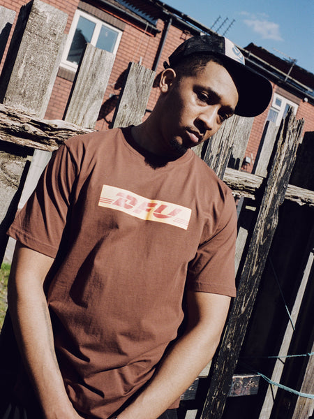 Lifestyle shot of a man wearing the Drama Call brown Shippin graphic tee