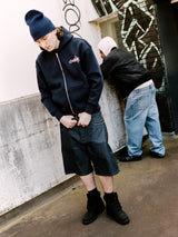 Model wearing a navy Drama Call Line-STA zip-up hoodie in an outdoor lifestyle shot.