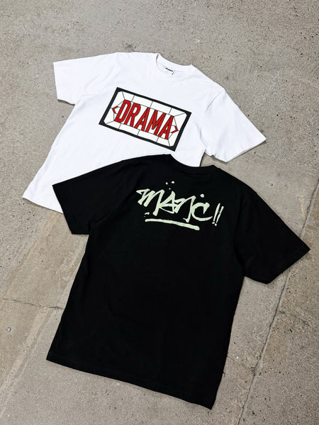 Men's white Drama Call Stained Glass graphic tee displayed in a flat lay view alongside a black tee on a textured surface.